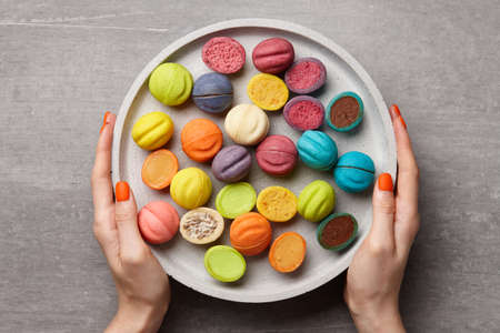 Woman holding concrete plate with colorful nut shaped desserts, top viewの写真素材