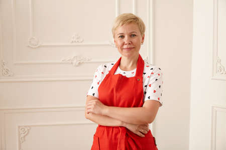 Woman in red apron holding glass bowl with colorful cookies in the kitchen, close up viewの写真素材