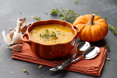 Pumpkin soup with thyme herb, cream and pumpkin seeds served in orange pumpkin shaped bowlの写真素材