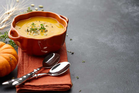 Pumpkin soup with thyme herb, cream and pumpkin seeds served in orange pumpkin shaped bowlの写真素材