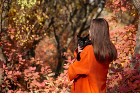 Young woman with black cat in park. Autumn seasonal.の写真素材