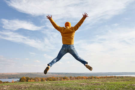 Happy man jumping to blue sky in field in sunny fall dayの写真素材