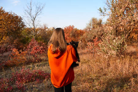 Young woman with black cat in park. Autumn seasonal.の写真素材