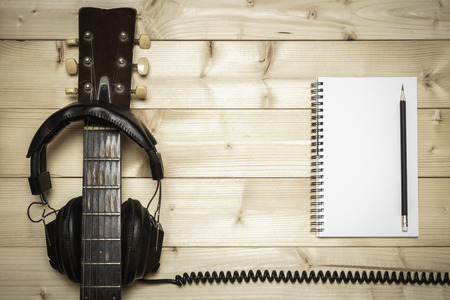 Old guitar on the wood background with notebook and headphonesの写真素材