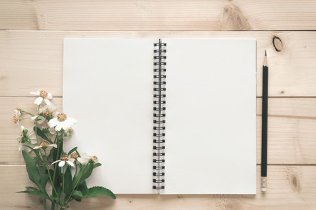 Notepad with pencil and grass flower on the wood background