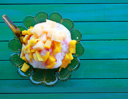 Shaved ice with fruits and syrup in the green glass cup on the green wood table.の写真素材