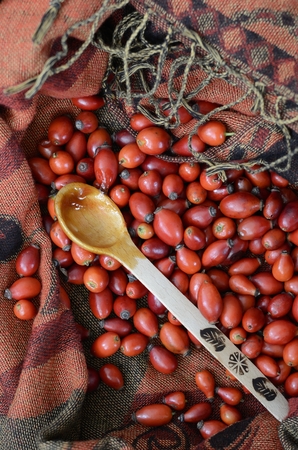 Rosehip berries and a wooden spoon with jam on fabric terracotta colorの写真素材