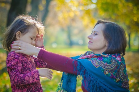 Beautiful and smiling mother cares about her daughter outdoor in fall seasonの写真素材
