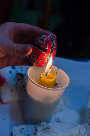 Easter eggs. Pysanka in hand above wax candle.の写真素材