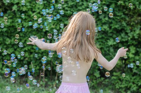 Girl plays and enjoys soap bubbles in the courtyardの写真素材