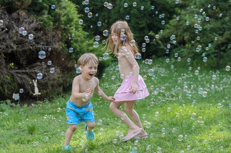 Girl and boy plays and enjoys soap bubbles in the courtyardの写真素材
