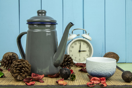 Gray metal teapot and white cup with white clock on wooden table background.の写真素材