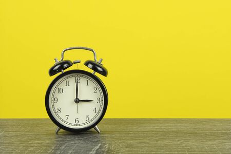 Black retro alarm clock on wooden table and yellow background. 