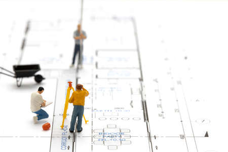 Miniature people surveyor technician is measuring the distance to build a house on drawing plan.