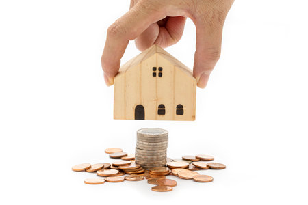 A woman's hand is holding a model wooden house on stack of coins on white background.の写真素材