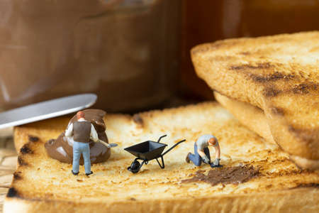 Miniature people are spreading chocolate on toast.