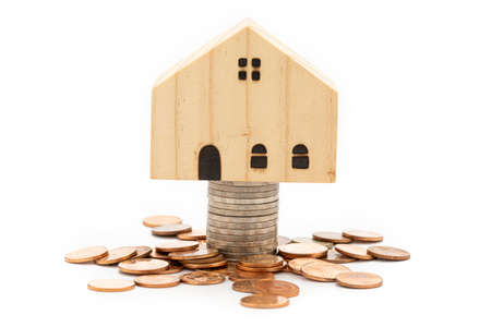 A model wooden house on stack of coins on white background.