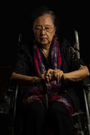 Asian elder woman in her wheelchair feeling lonely on black backgroundの写真素材