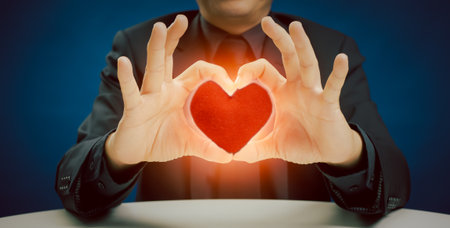 Businessman in suit showing hands sign gesture with red heart shape pillow on blue background in the studio. take care of health, being in love and service mind business conceptの写真素材