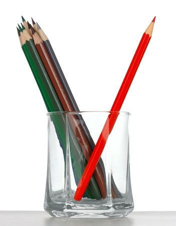 Crayons in a glass, red one is leaned against the others, standing out of the crowd concept, isolated over whiteの写真素材