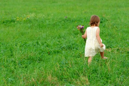 Little girl walk on green meadow with bouquet of field flowersの写真素材