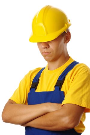 Serious young worker pull hardhat over his eyes, wearing blue-and-yellow uniform, isolated on whiteの写真素材
