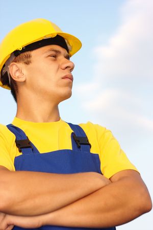 Portrait of a young construction worker, dressed in blue-and-yellow uniform and hard hat, over blue skyの写真素材