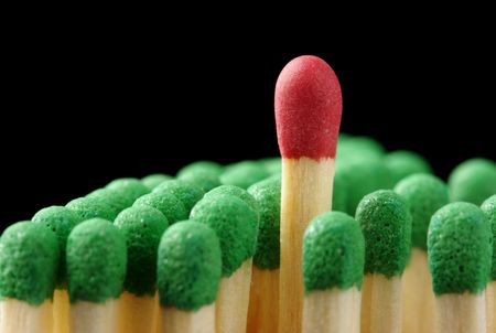Single red matchstick among green ones, out of the crowd concept, isolated over blackの写真素材