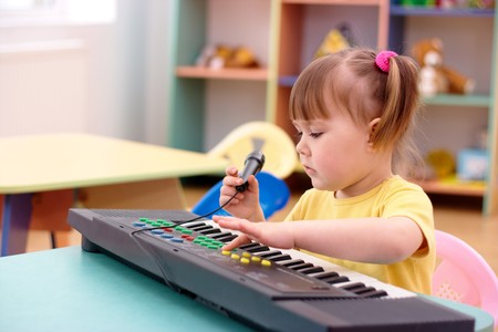Little girl with electronic piano and microphone in preschoolの写真素材