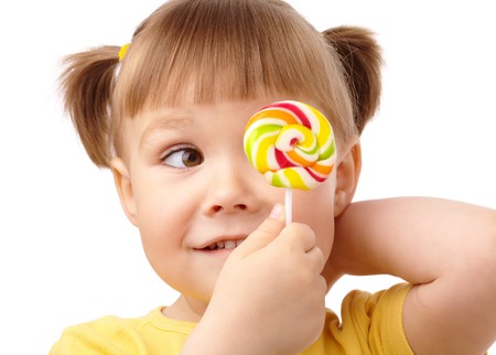 Cute little girl is looking at her colorful lollipop, isolated over whiteの写真素材