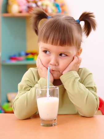 Gloomy little girl drinks milk in preschoolの写真素材