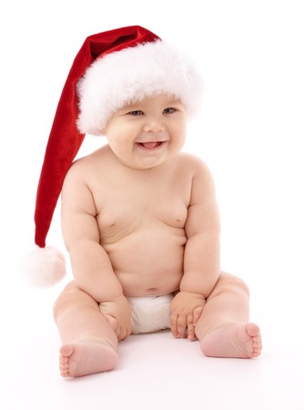 Adorable child is sitting on floor, wearing red Christmas cap, isolated over whiteの写真素材