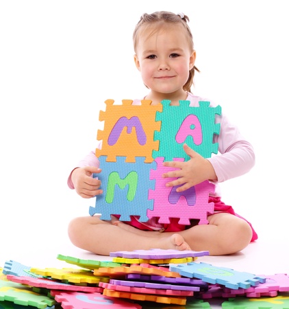 Cute little girl is playing with alphabet while sitting on floor, isolated over whiteの写真素材