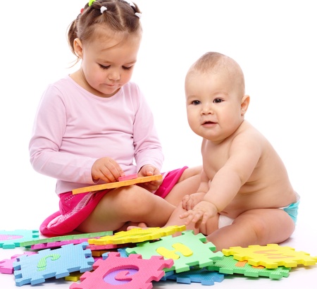 Cute little boy and girl are playing with alphabet while sitting on floor, isolated over whiteの写真素材