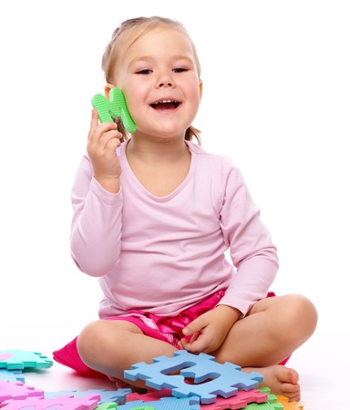 Cute little girl is playing with alphabet while sitting on floor, isolated over whiteの写真素材