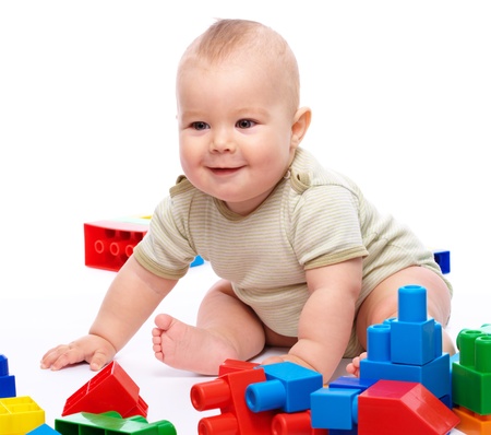 Cute little boy is playing with building bricks while sitting on floor, isolated over whiteの写真素材