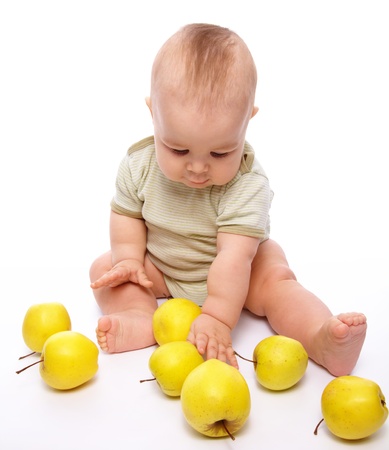 Cute little boy is playing with few yellow apples while sitting on floor, isolated over whiteの写真素材