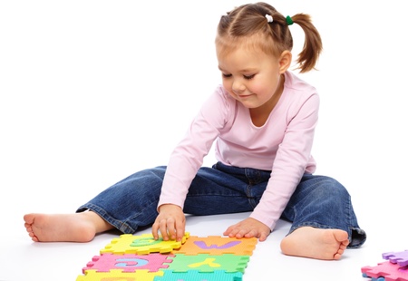 Cute little girl is playing with alphabet, putting hands up while sitting on floor, isolated over whiteの写真素材