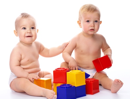 Two children are playing with building bricks while sitting on floor, isolated over whiteの写真素材