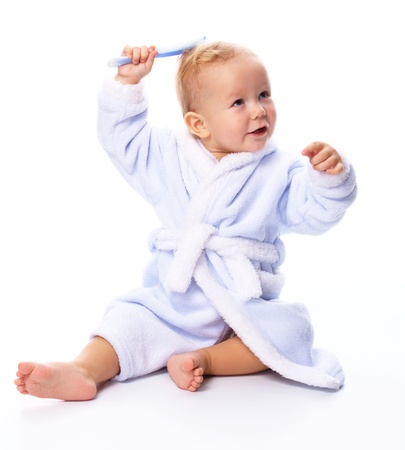 Bright portrait of a cheerful child in blue bathrobe combing his hair, isolated over whiteの写真素材