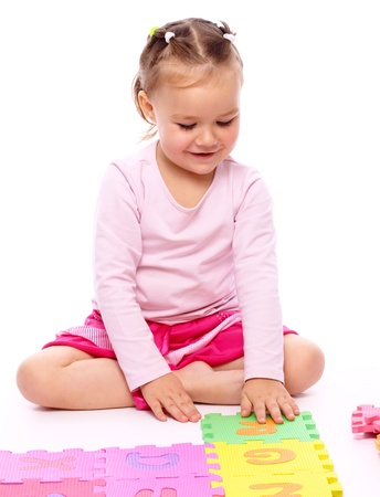 Cute little girl is playing with alphabet while sitting on floor, isolated over whiteの写真素材