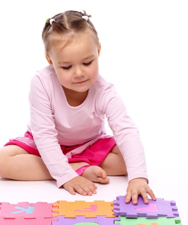 Cute little girl is playing with alphabet while sitting on floor, isolated over whiteの写真素材