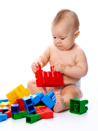Cute little boy is playing with building bricks while sitting on floor, isolated over whiteの写真素材