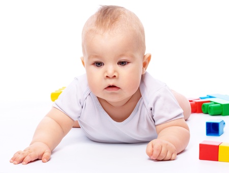 Cute little boy is playing with building bricks while sitting on floor, isolated over whiteの写真素材