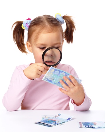Cute little girl is looking at twenty euro banknote using magnifier, isolated over whiteの写真素材