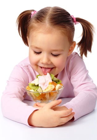 Cute little girl licks fruit salad, isolated over whiteの写真素材