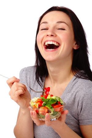 Young attractive woman eats vegetable salad using fork, isolated over whiteの写真素材