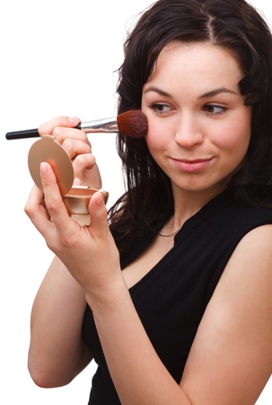 Young attractive girl is applying rouge using brush while looking at mirror, isolated over whiteの写真素材