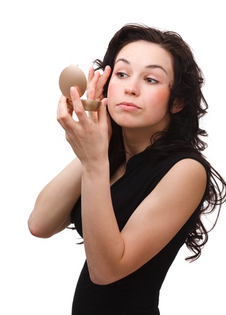 Young attractive girl is applying makeup while looking at mirror, isolated over whiteの写真素材