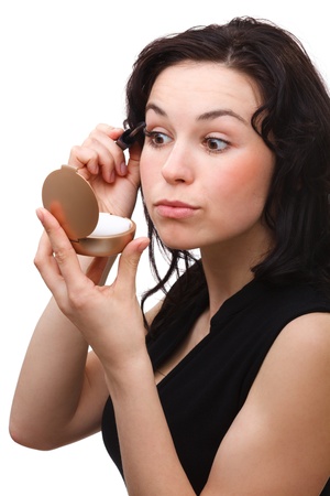 Young woman is applying mascara while looking at herself in mirror, isolated over whiteの写真素材